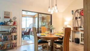 A dining area with a wooden table, chairs, and a chandelier. There is a bookshelf with books and decorative items. - Lake House in Centerville with Private Water Access! (Barnstable)