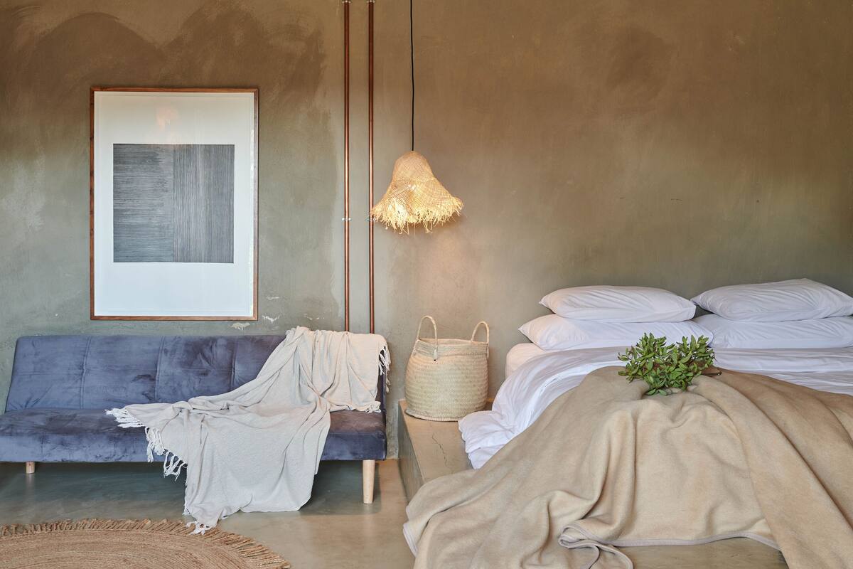 A bedroom with a bed, a sofa, a lamp, and a framed picture on the wall.