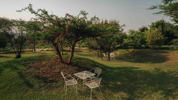 An outdoor seating area with metal chairs and tables, surrounded by trees and grass.