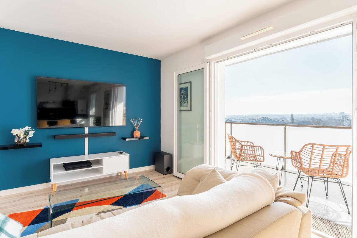Uma sala de estar moderna com uma televisão grande, um sofá e uma varanda com cadeiras laranja.