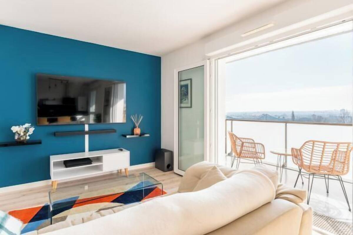 A modern living room with a large TV, a sofa, and a balcony with chairs.