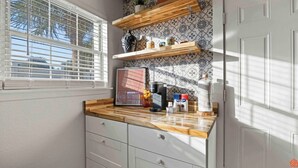 Una cocina con mostradores de madera, una cafetera y un ventanal con persianas.