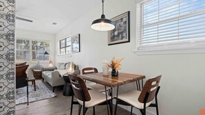 Un comedor con una mesa y sillas de madera, una lámpara colgante y una obra de arte enmarcada en la pared.