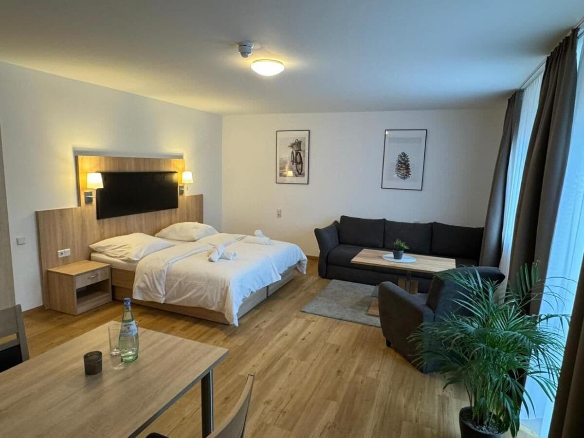 Una habitación de hotel moderna con cama, sofá, una mesita y televisor.