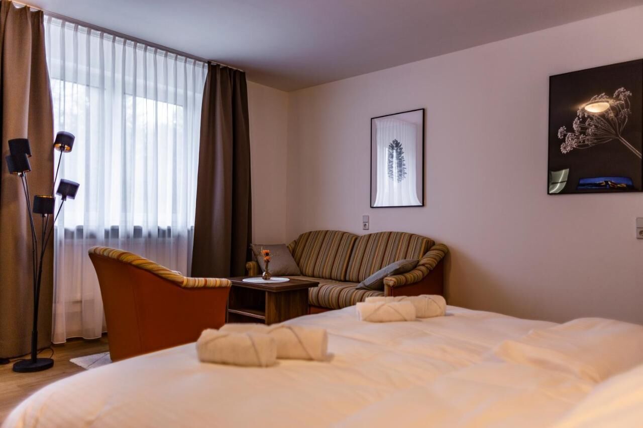 A hotel room with a bed, a sofa, a small table with a vase, and a lamp.