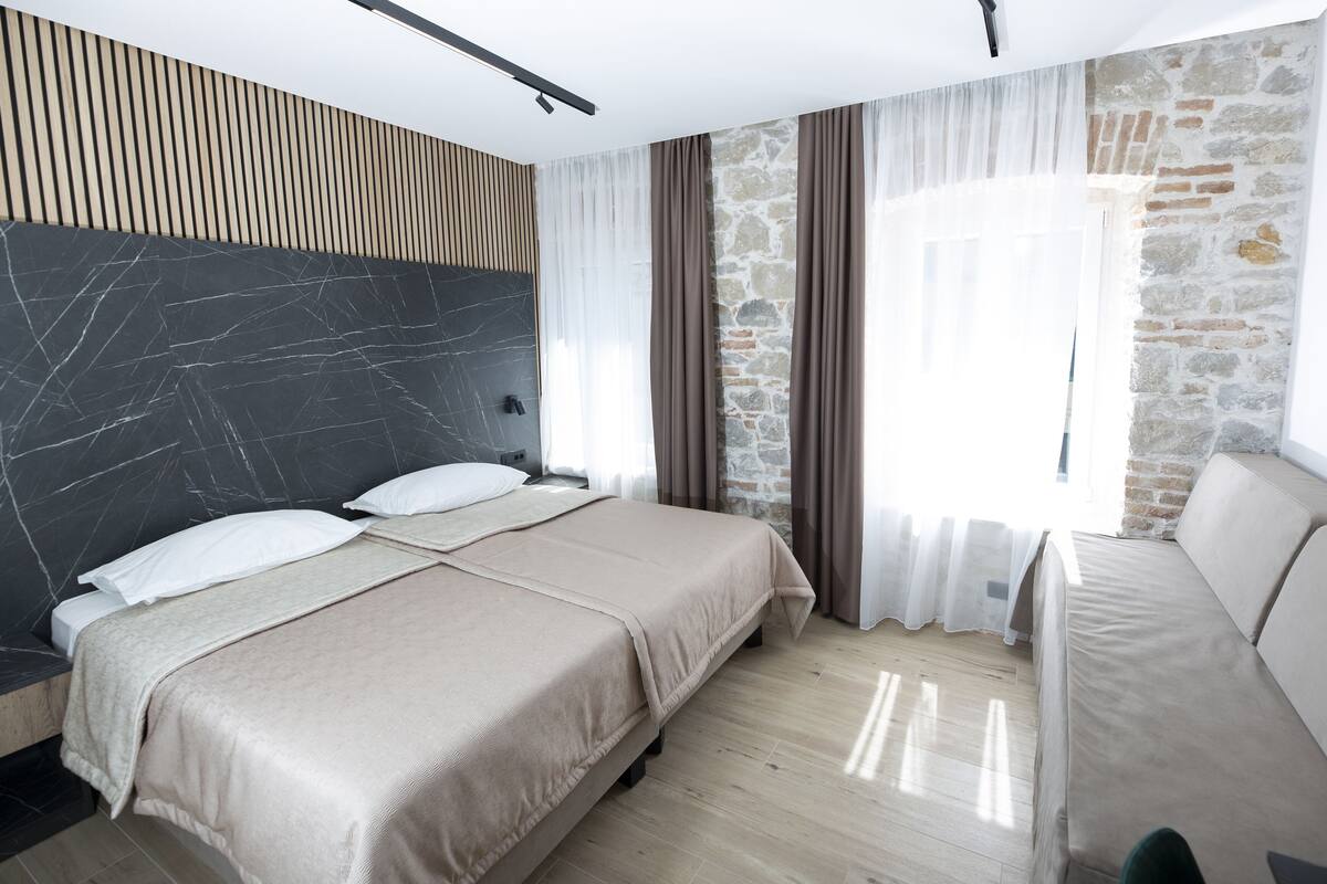A modern hotel room with a large bed, a sofa, and a stone accent wall.