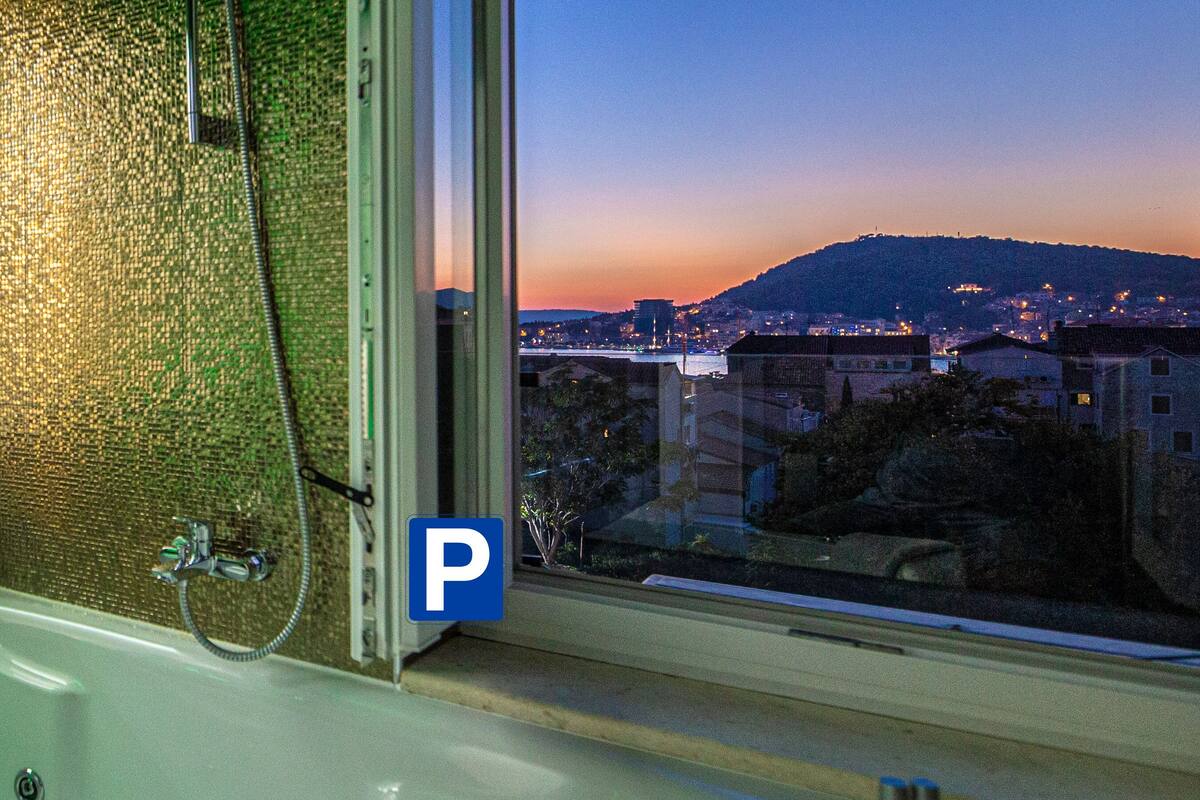 A bathroom with a bathtub, a shower, and a view of a cityscape at dusk.