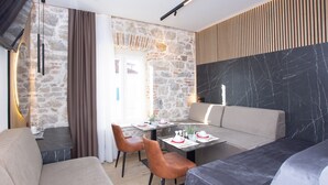 A modern dining area with a stone wall, a black marble accent wall, and a wooden slatted wall. There are dining tables with chairs, a sofa, and a small table with a lamp. - A Heritage Hotel Split (Split)