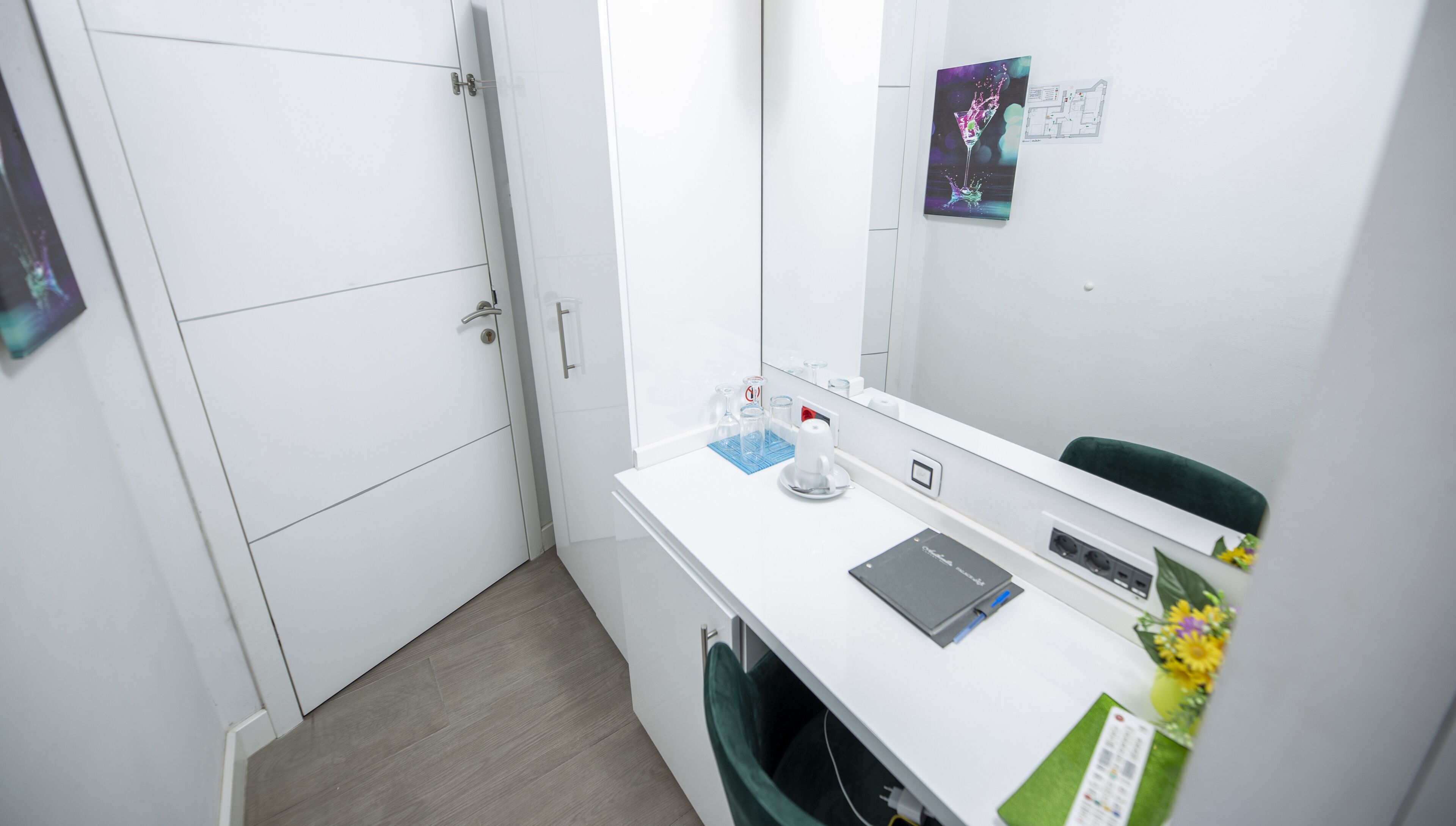 A hotel room with a white desk, a mirror, a trash bin, and a small green plant.