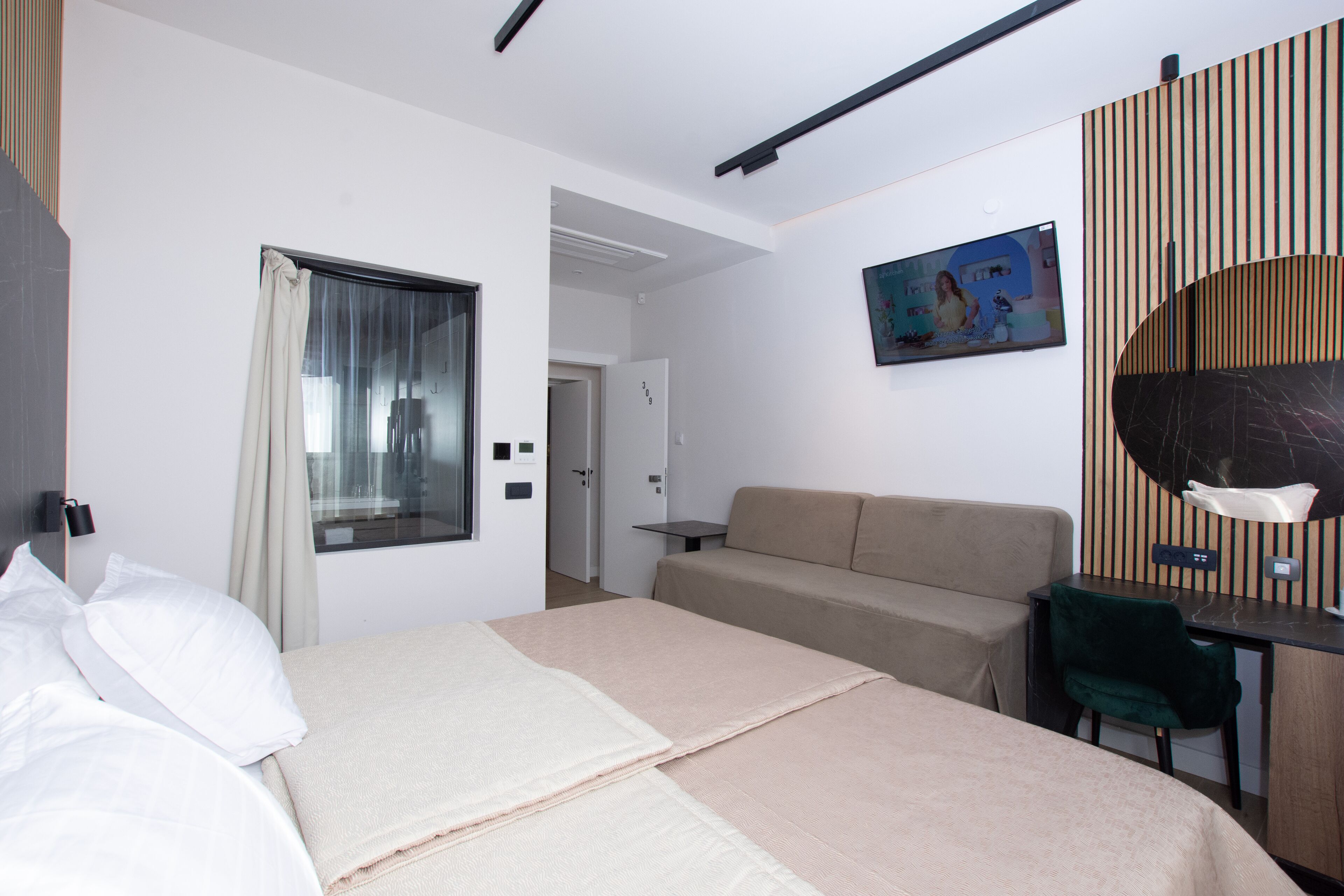 A modern hotel room with a bed, a sofa, a desk, and a TV.