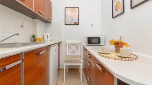 A compact kitchen with wooden cabinets, a white countertop, a microwave, a sink, and a chair. - Apartment in the center of Warsaw | Balcony and Workspace (Warszawa)