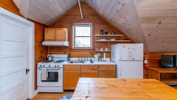 A compact kitchen with wooden cabinets, a stove, a sink, and a refrigerator.