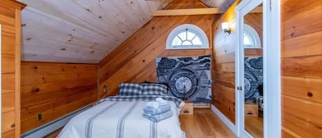 A bedroom with a sloped ceiling, wooden walls, a bed with a striped blanket, and a tapestry on the wall.
