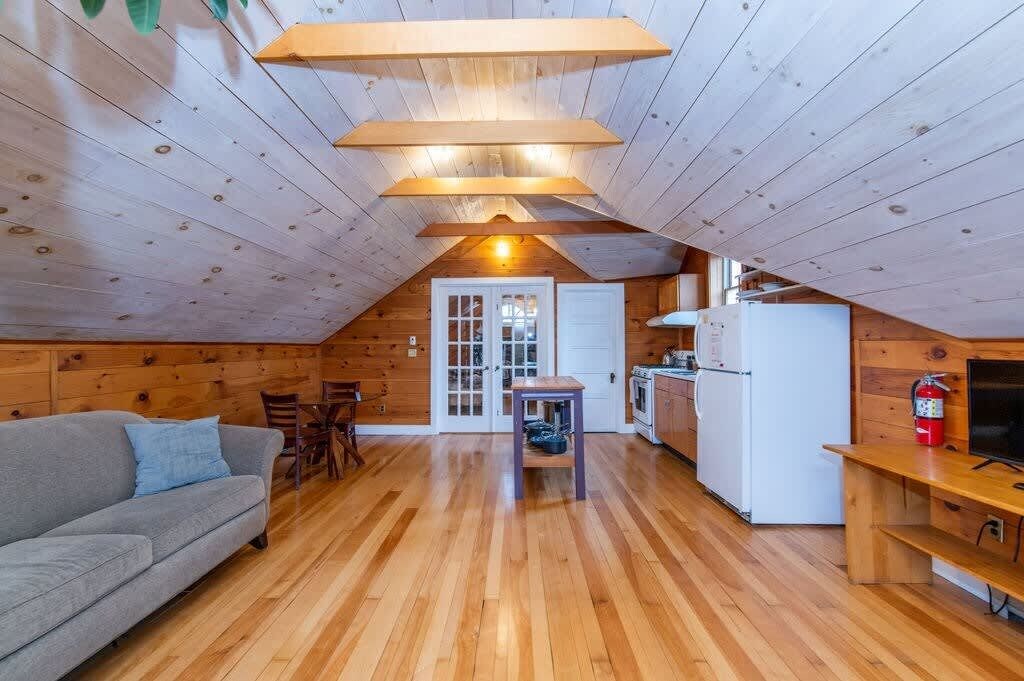Een gezellig zolderkamertje met houten plafond, een bank, een eettafel en een kitchenette.