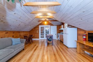Acogedor dormitorio en ático con piso de madera, un sofá gris, una mesa de comedor y una zona de cocina con refrigerador y estufa.