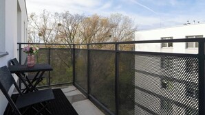 Een balkon met een gaashek, een tafel en twee stoelen.