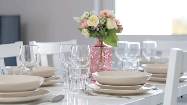 Een eettafel gedekt met borden, glazen en een vaas met bloemen.