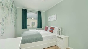 Een slaapkamer met een bed, nachtkastjes, een raam met gordijnen en een uitzicht op een gebouw.
