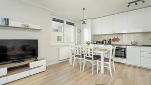 Een moderne keuken met witte kastjes, een eettafel met stoelen, een inbouwoven en een tv op een witte console.
