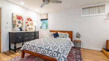 A bedroom with a bed, a dresser, a ceiling fan, and artwork on the walls.
