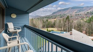 Ein Balkon mit Stühlen, einer Uhr und Blick auf eine gebirgige Landschaft mit Gebäuden.
