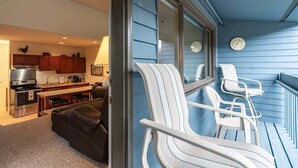 Eine moderne Küche mit Edelstahlgeräten, ein Essbereich mit Tisch und Stühlen sowie ein Balkon mit weißen Stühlen.