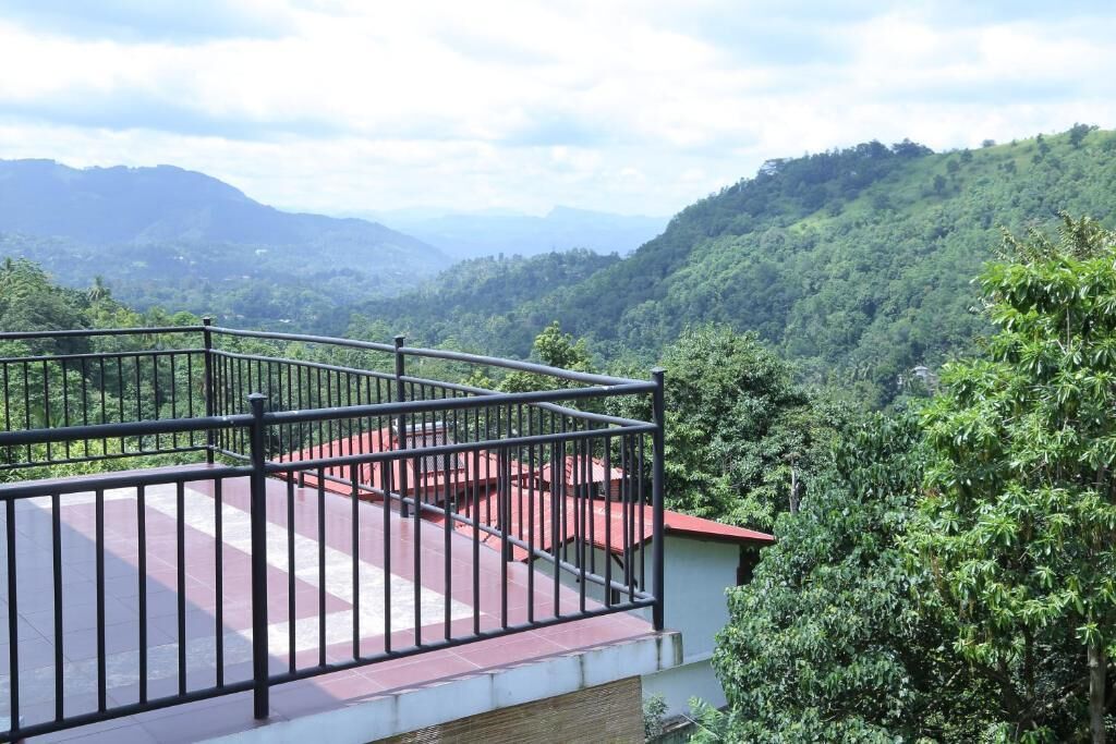 A balcony with a metal railing overlooking a lush green valley with distant mountains.
