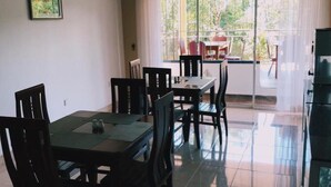 Un coin repas avec une table et des chaises, une fenêtre donnant sur un espace verdoyant et une porte-fenêtre coulissante qui mène à un espace extérieur.