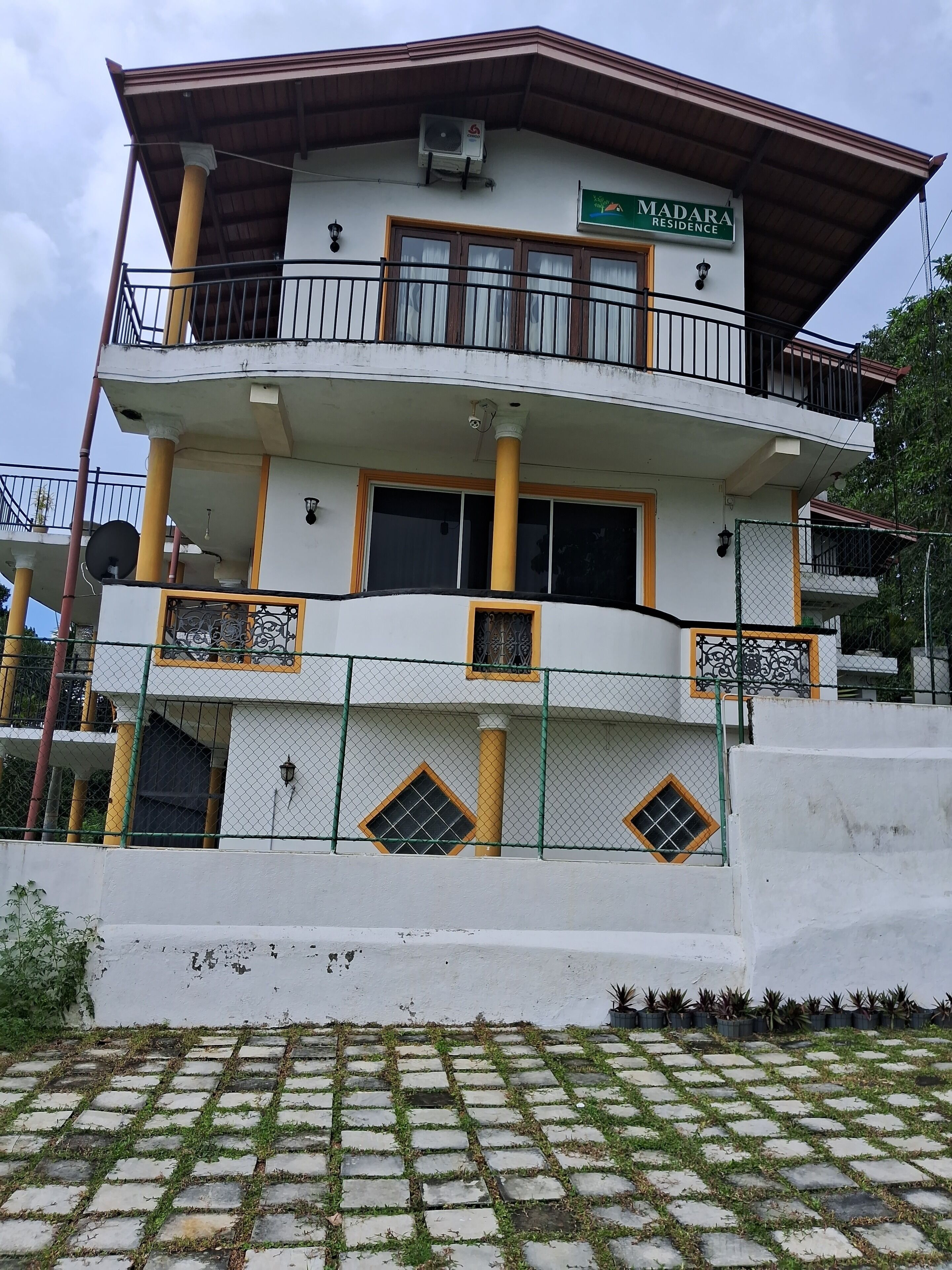 A multi-story building with balconies, a sign reading "MADARA RESIDENCE," and a satellite dish.