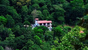 Un bâtiment à deux étages, surmonté d’un toit rouge, entouré d’une forêt dense et verdoyante.