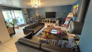 Ein Wohnzimmer mit Sofa, Couchtisch und Fernseher. Es gibt eine Essecke mit Tisch und Stühlen. Die Wand ist blau und es gibt ein Fenster.