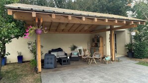 Ein überdachter Patio-Bereich mit einer Holz-Pergola, Sitzmöbeln und Topfpflanzen.
