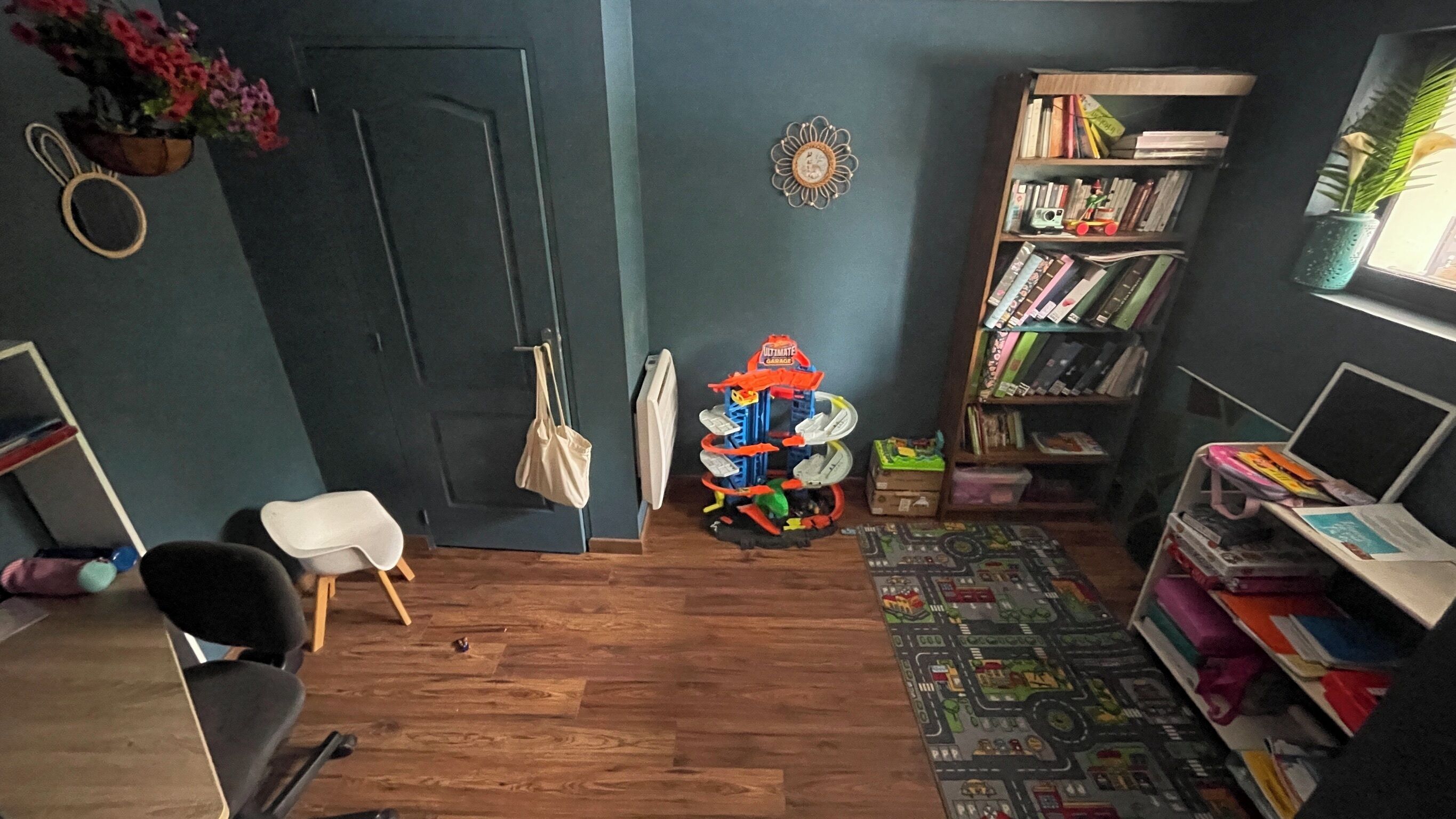 Ein Zimmer mit Holzboden, einem Bücherregal, einem Schreibtisch, einem Stuhl, einem kleinen Spielzeugauto und einem Blumentopf.