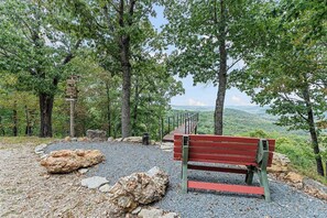 A bench with a metal railing, surrounded by trees and a rocky ground.
