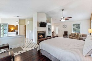 A bedroom with a large bed, a fireplace, a ceiling fan, and a view of the living area.