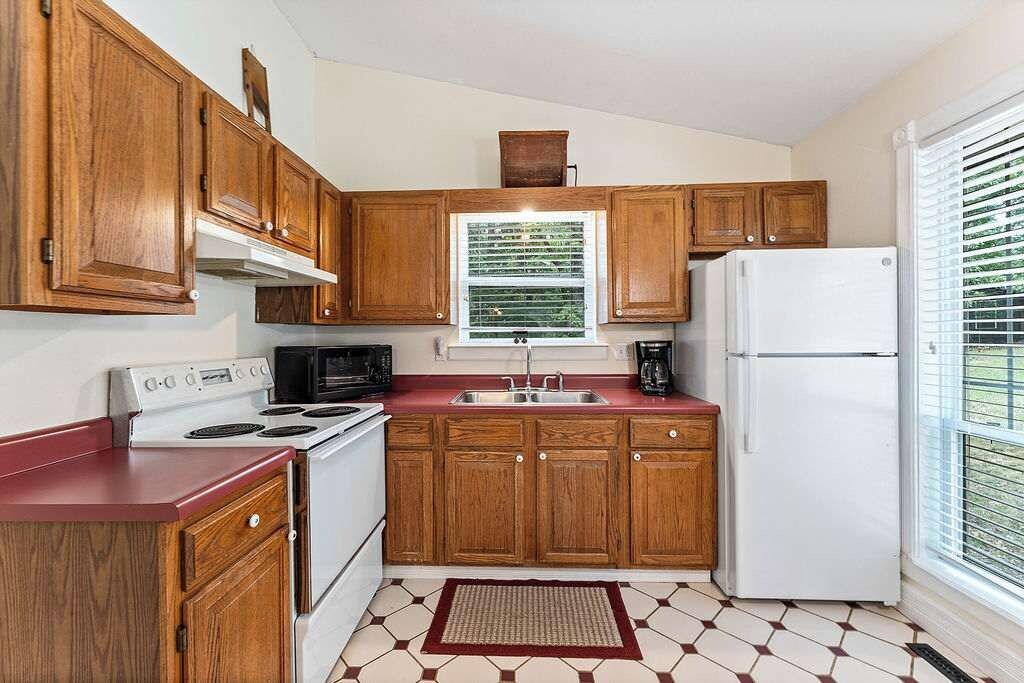 A kitchen with wooden cabinets, a white stove, a microwave, and a refrigerator.