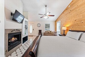 Una habitación de hotel con chimenea, una cama, un ventilador de techo y un televisor.