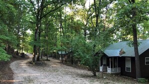 Un chemin de gravier mène à une rangée de cabanes dotées d’une véranda, le tout étant entouré d’arbres.