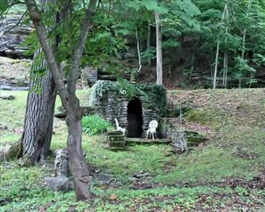 Une construction rustique en pierre, dotée d’une entrée en arc de cercle, et entourée d’une végétation luxuriante et d’arbres.