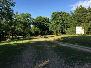 Un chemin de gravier bordé d’arbres et un panneau indicateur.
