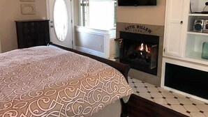 Une chambre à coucher avec une couvre-lit à motifs, une cheminée, un téléviseur et un meuble contenant une radio.