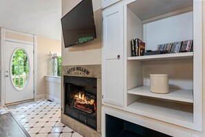 Een open haard met daarboven een televisie, een boekenplank vol boeken, en een deur met een rond raam.