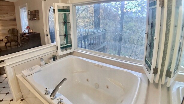 Une salle de bain avec une grande baignoire, une fenêtre donnant sur la forêt et un mur en bois.