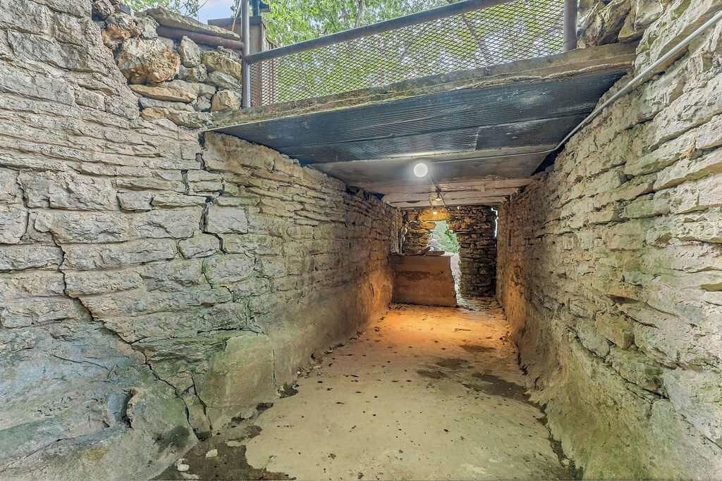 A narrow stone passageway with a wooden ceiling and a metal railing on top.