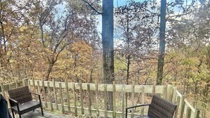 Une terrasse en bois avec deux fauteuils en osier et une table, entourée d’une clôture en bois et d’arbres.