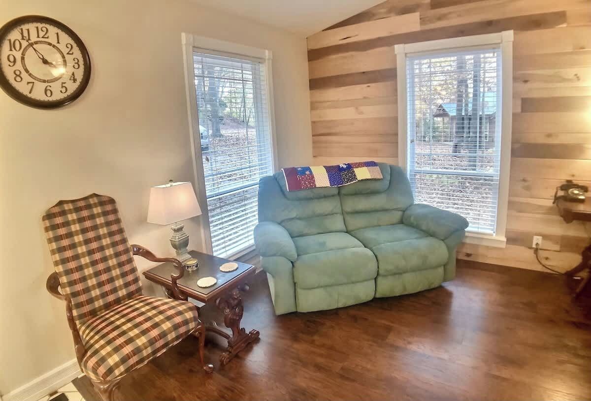 Un salon avec un fauteuil à motifs écossais, un canapé turquoise, un plancher en bois et une horloge murale.