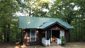 Une petite cabane dotée d’un porche, entourée d’arbres.
