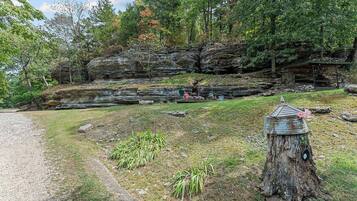A natural landscape with a rocky cliff, a wooden structure resembling a birdhouse, and a gravel path.