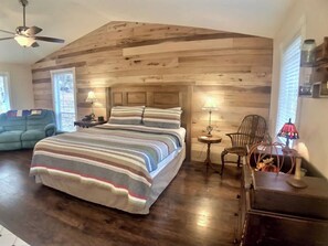 A bedroom with a large bed, wooden ceiling, a small table, a chair, and a lamp. - Secluded Eureka Cabin | King | Mountain Spa Tub (Eureka Springs)