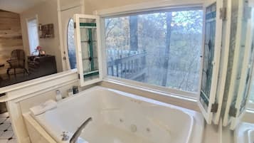 Une salle de bain avec une grande baignoire, une fenêtre donnant sur la verdure et un miroir avec un cadre vert.